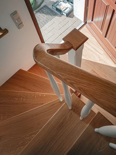 Eichenstufen mit weiß lackierten Geländerstäben – eine aufgesetzte Holztreppe, auf Betonstufen. Blick nach unten auf die Stufen.