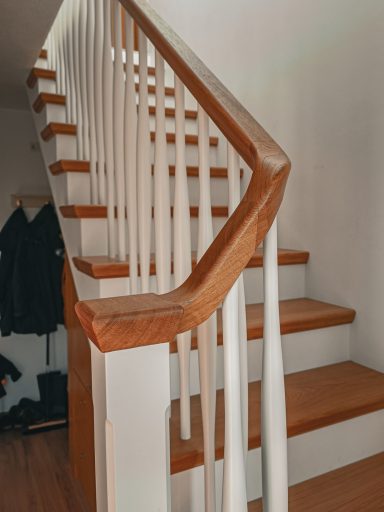 Eichenstufen mit weiß lackierten Geländerstäben – eine aufgesetzte Holztreppe, auf Betonstufen. Blick auf den Posten